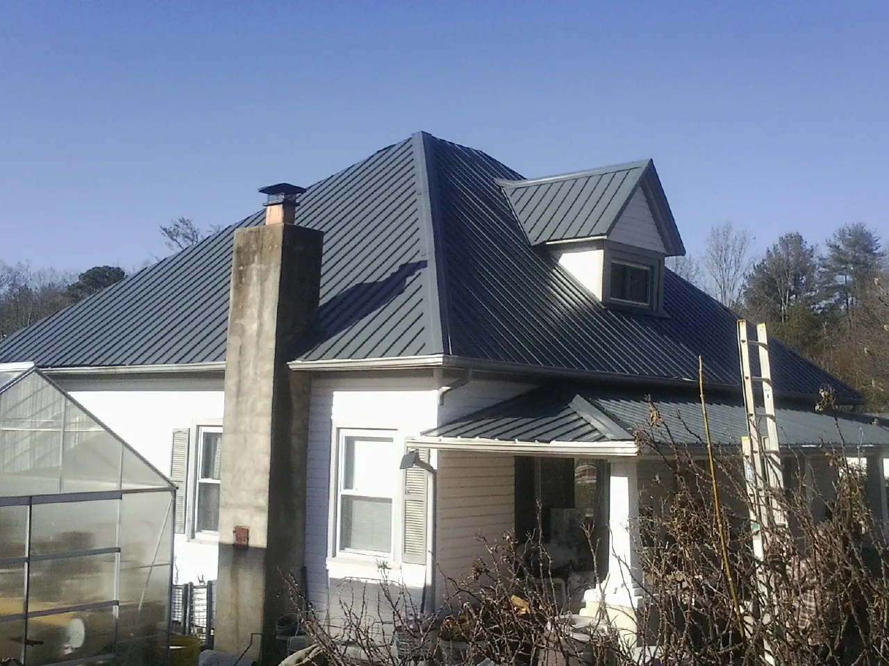 Dark blue standing seam metal roof on a white farmhouse with dormer — Slate & Tile Roof Repair by Roofing Brothers in Wells Bridge