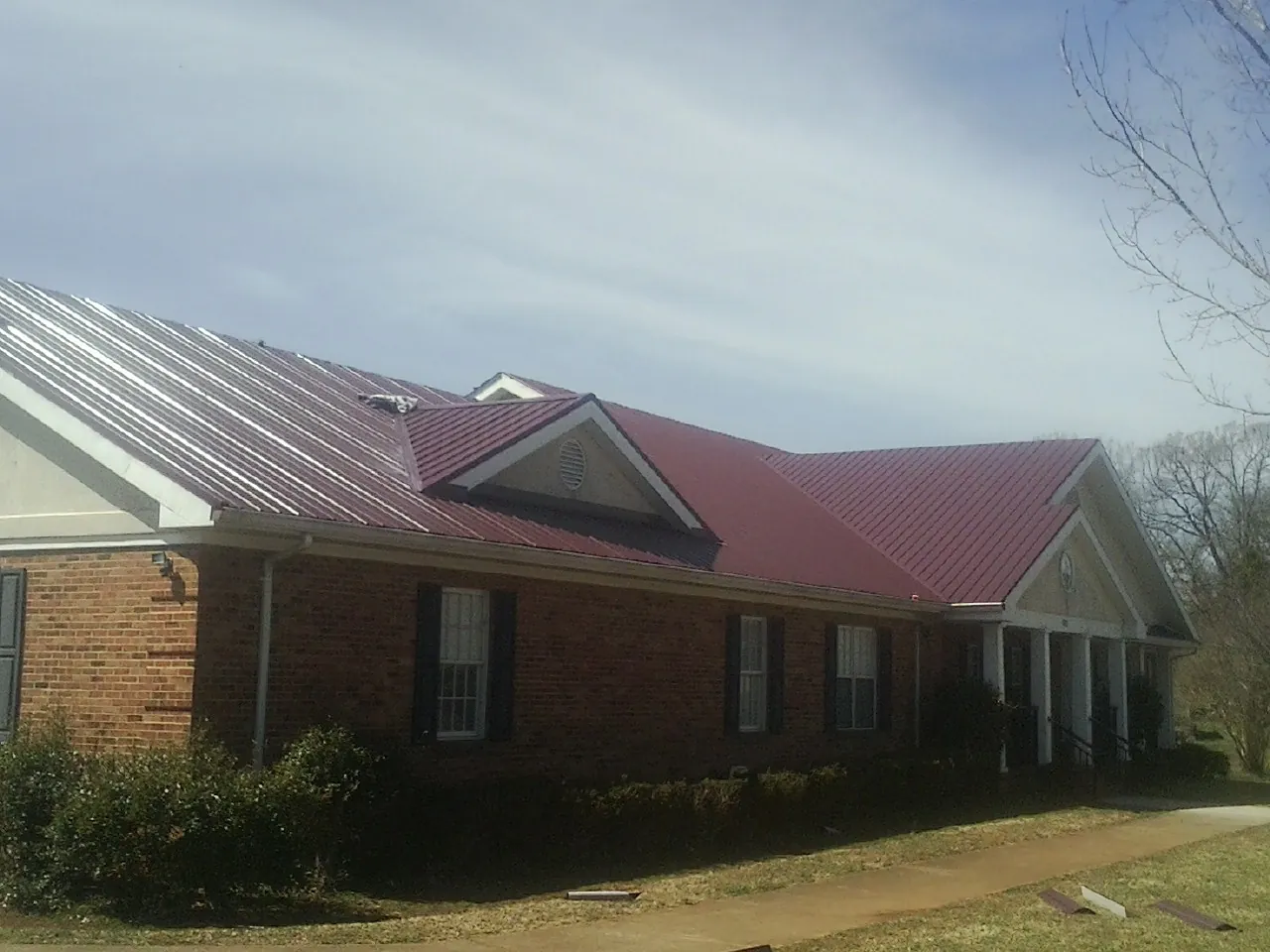 Red metal roof with gabled entries on a long brick building, from a Hail Damage Roof Repair job in Wells Bridge