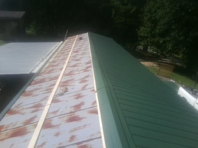 Old rusted panels beside newly installed green metal roofing — Wind Damage Roof Repair by Roofing Brothers in Wells Bridge