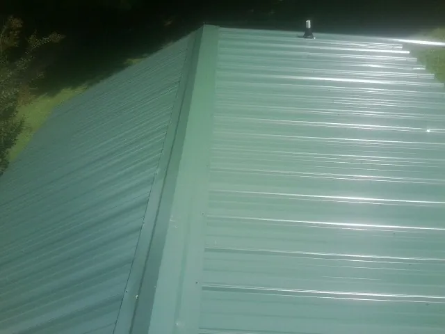 New green metal panels meeting at the ridge of a roof — Flat Roof Repair work by our crew in Wells Bridge