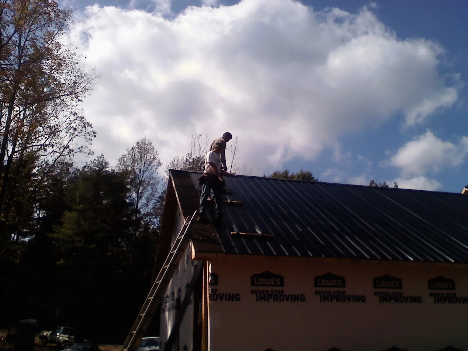 Roofer fastening dark metal panels high against a cloudy sky, from a Roof Inspection job in Wells Bridge
