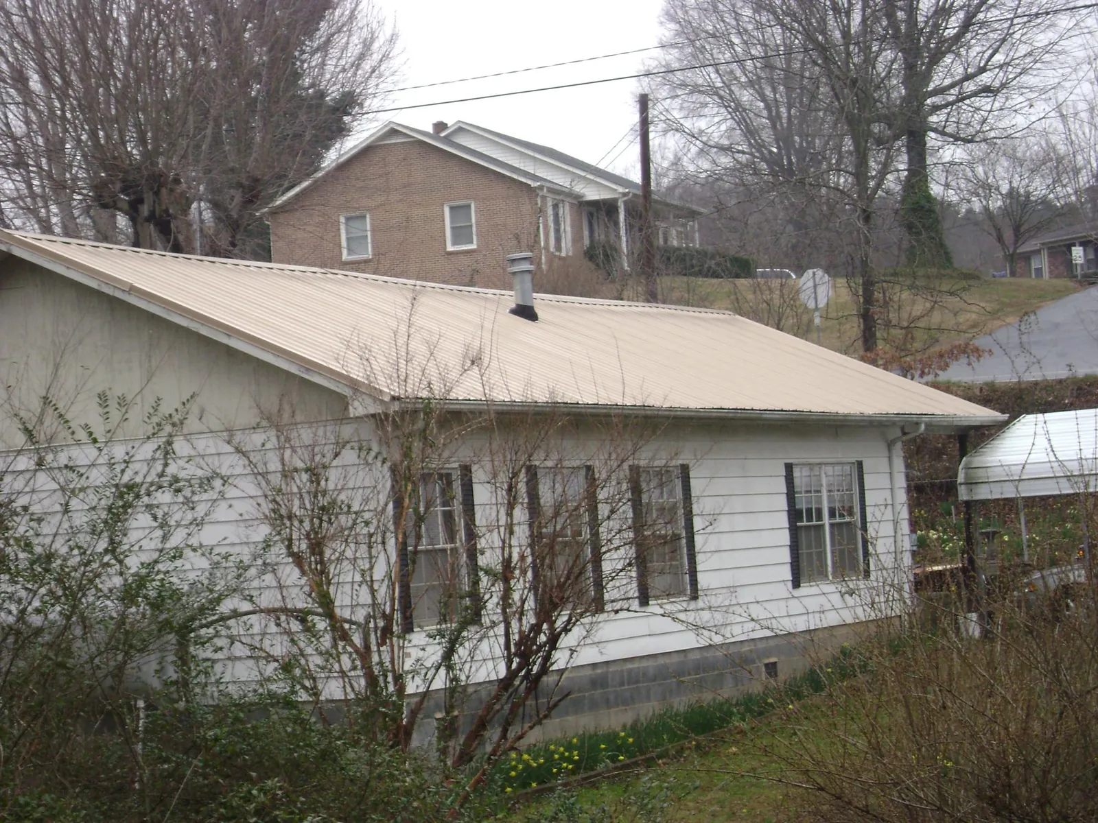 Tan metal roof on a white sided house set into a hillside — Commercial Roofing by Roofing Brothers in Wells Bridge