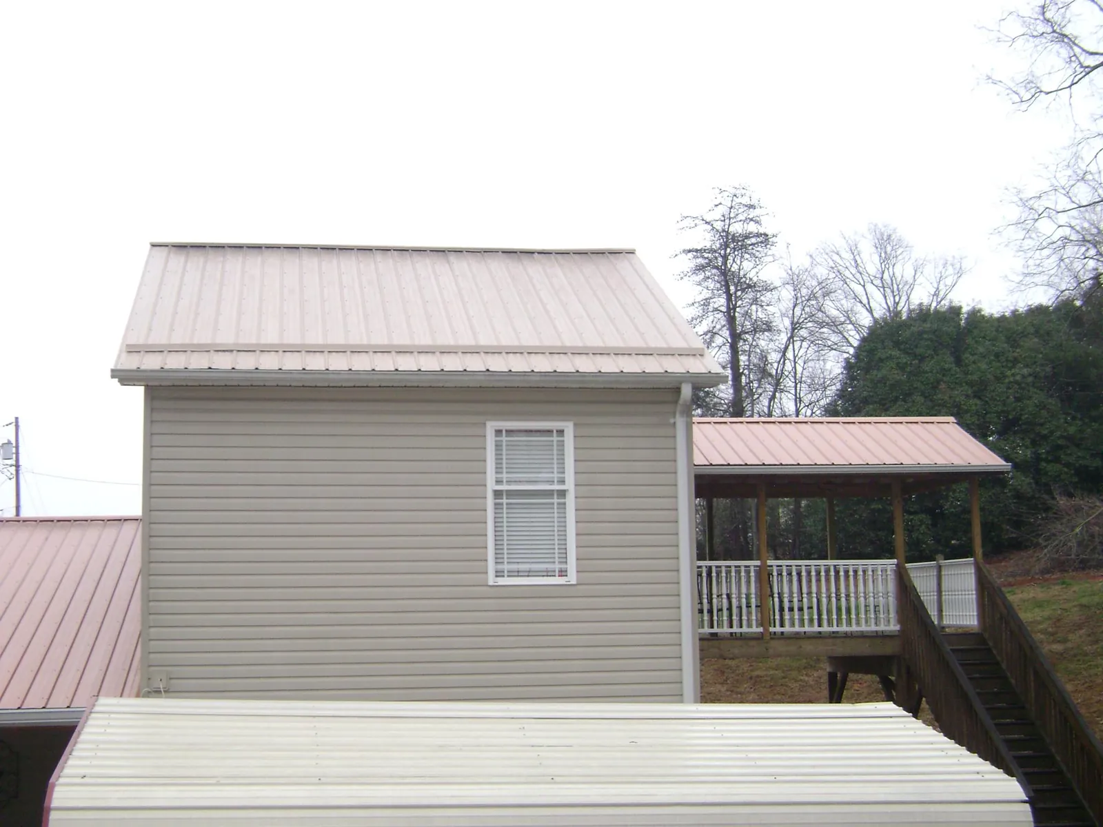 Tan metal roofs on a two story addition and attached porch, from a Roof Replacement job in Wells Bridge