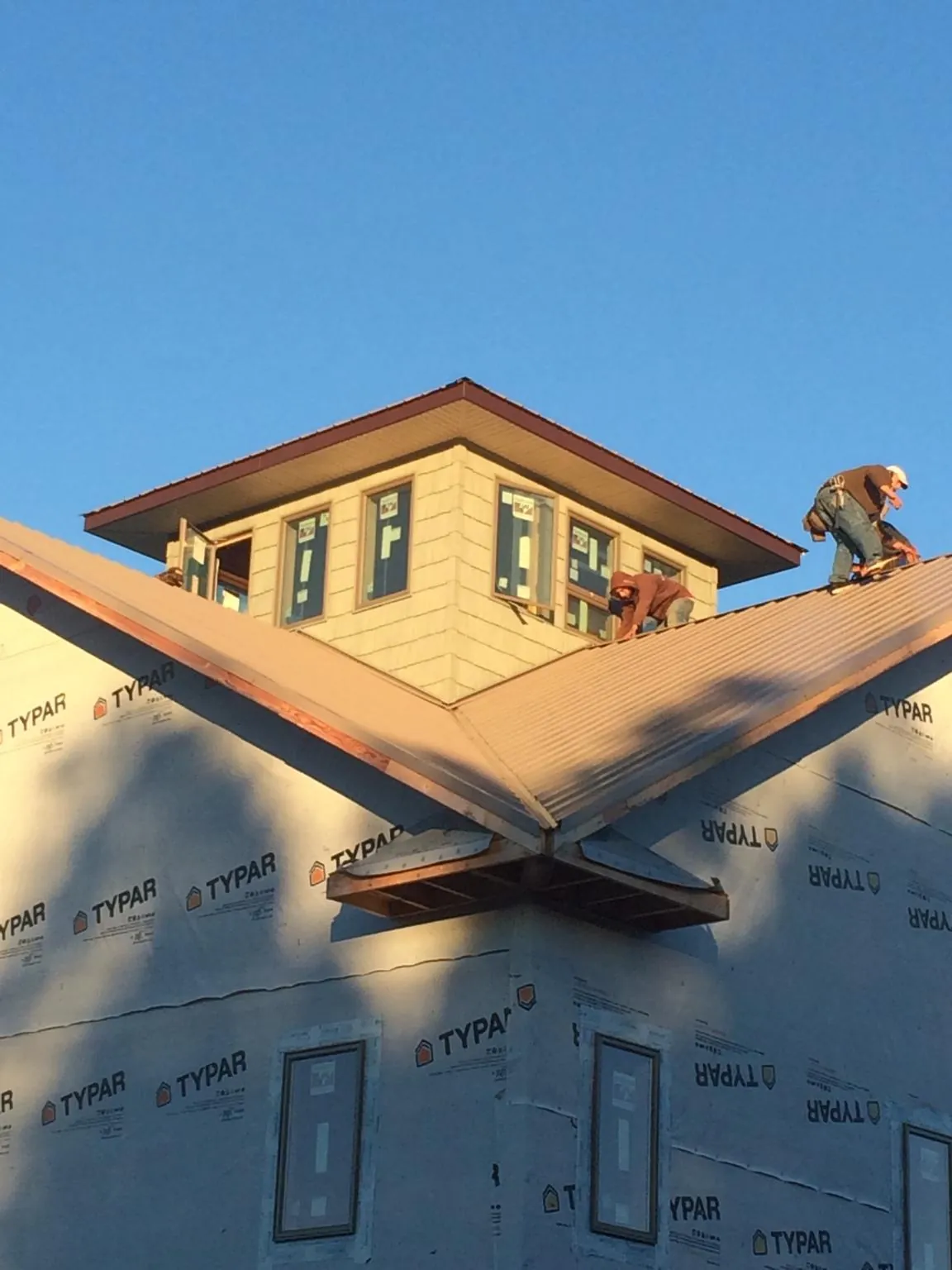 Roofers working around a rooftop cupola on a new metal roof at sunset — Roof Waterproofing in Wells Bridge by Roofing Brothers